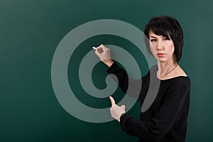 Strict teacher posing by chalk Board, learning concept, green background, Studio shot