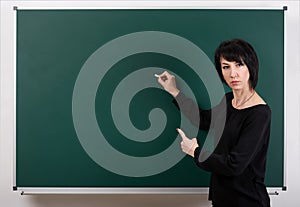 Strict teacher posing by chalk Board, learning concept, green background, Studio shot