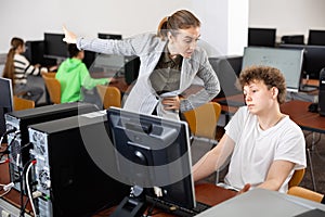 Strict teacher reprimanding negligent teenage student in computer class