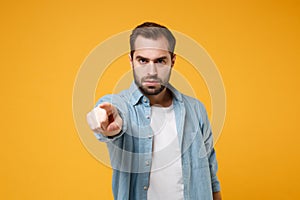 Strict young bearded man in casual blue shirt posing isolated on yellow orange background wall studio portrait. People