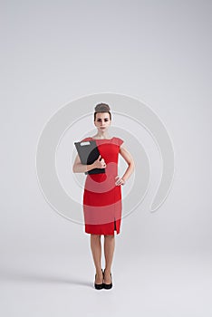 Strict young businesswoman in red dress holding folder