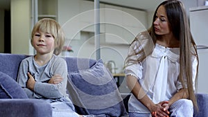 Strict young mother and stubborn son sitting on couch at home talking. Portrait of Caucasian woman scolding boy with
