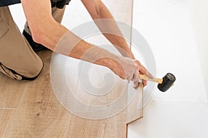 Strikes with a soft hammer on the part with a lock, for fixing. Installing laminate flooring fitting the next piece -