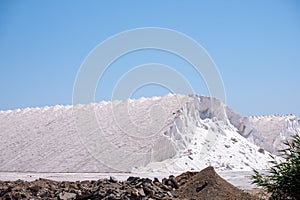 A striking contrast of white salt mounds against a clear sky, with rough earth in the foreground emphasizing the mining