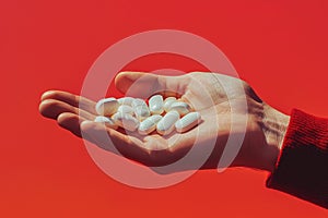 Close-up view of white pills in a human hand on a bold red background photo