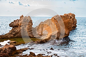 Majestic Coastal Rock Formation by the Sea With Dramatic Textures and Colors Under a Cloudy Blue Sky, Perfect for Travel and photo