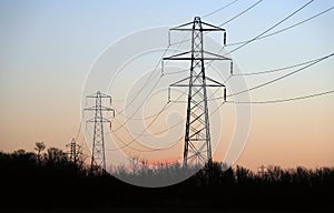 A striking sunrise shot of electricity pylons supporting overhead power lines in an orange sky.