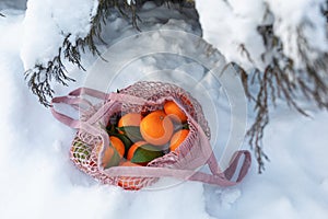 A string bag full of tangerines on the snow under the Christmas tree