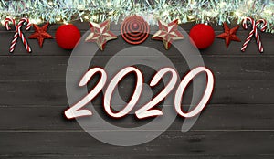 A string of christmas star decorations, lights and tinsel, with 2020 written in the middle, on destressed dark wood