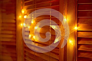 a string of christmas stars in front of a window, against a wooden wall