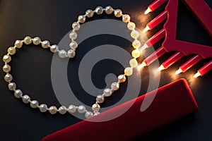 A string of pearls on a black background, burning lights, a red box. St. Valentine`s Day