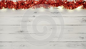 A string of red and silver christmas lights and tinsel, on destressed white wood