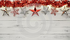 A string of red and silver christmas star decorations, lights and tinsel, on destressed white wood