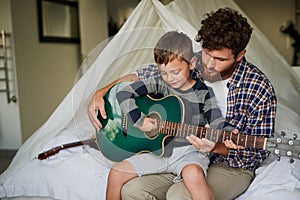 String by string. Cropped shot of an adorable little boy sitting on his dads lap while learning to play the guitar at