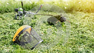 String trimmer and protective face mask on mown grass, sunlight, banner 16x9 format