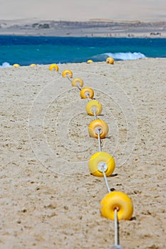 String of yellow marker buoys on sandy beach