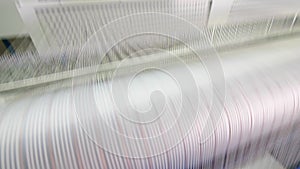 Strings of white threads are rapidly relocating. Textile factory equipment.