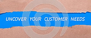 A strip of blue paper with the words UNCOVER YOUR CUSTOMER NEEDS between the brown paper. View from above