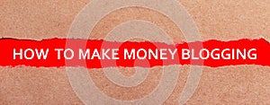 A strip of red paper under the torn brown paper. White lettering on red paper HOW TO MAKE MONEY BLOGGING. View from above