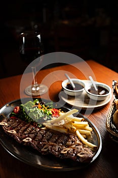 Strip roast with french fries and salad on wooden table with glass of red wine. Argentine restaurant concept. Gastronomy concept