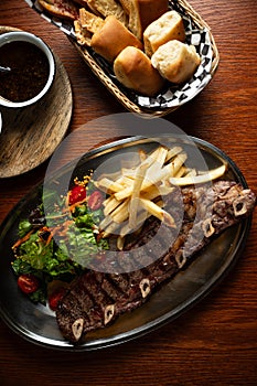 Strip roast with french fries and salad on wooden table with glass of red wine. Argentine restaurant concept. Gastronomy concept.