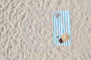 Striped beach towel with straw hat, book, sunglasses and slippers on sand, aerial view. Space for text