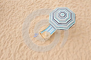 Striped beach umbrella near sunbed with vacationist`s stuff on sandy coast, aerial view