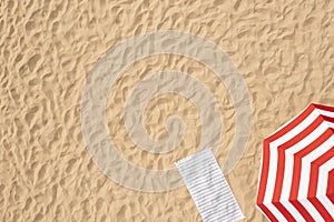 Striped beach umbrella near towel on sand, aerial view. Space for text