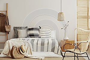 Striped bedding on king size bed in contemporary bedroom interior with wicker chair and copy space on empty wall