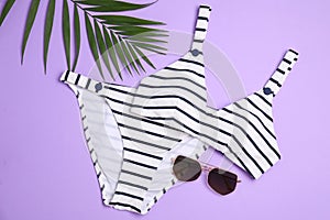 Striped bikini, sunglasses and green leaf on background, flat lay. Beach objects