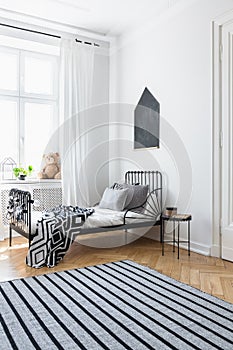 Striped carpet in white bedroom interior with patterned blanket on bed near window