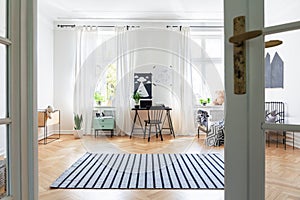 Striped carpet on wooden floor in spacious kid`s room interior with chair at desk and posters