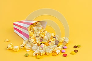 Striped carton bucket with caramel popcorn and dragee candies on yellow background