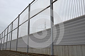 Striped glass noise barrier made of metal perforated sheet metal slats. gray and silver protective fencing separates housing from