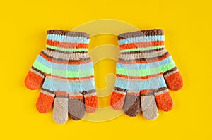 Striped kids winted gloves composition on yellow background