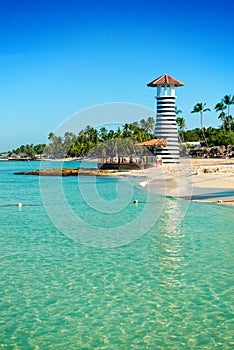 Striped lighthouse on sandy shore with palm trees.