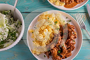 Striped meat with cream sauce and pasta and salad on wooden table. Flat lay