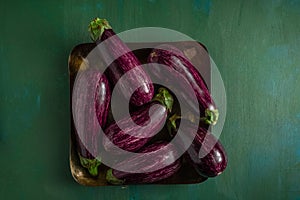 Striped purple eggplants in square platter on dark green background