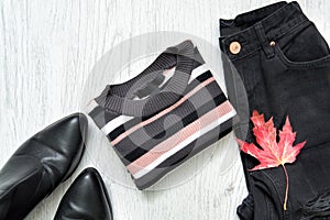 Striped sweater, black jeans, boots and red maple leaf. Fashionable concept