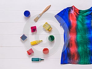 A striped tie dye t-shirt and paint on a white wooden background. Flat lay