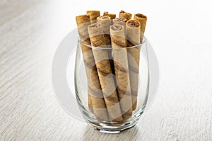 Striped wafer rolls with chocolate filling in drinking glass on wooden table