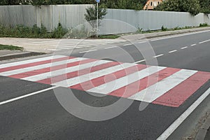 Striped white red pedestrian crossing on gray asphalt road