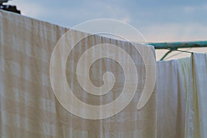 Striped yellowish white bedding hangs on a clothesline after washing. A concept about household chores, from which it is