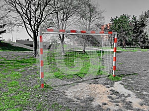 Stripped red and white ball game goal net in the park with sparsely green grass