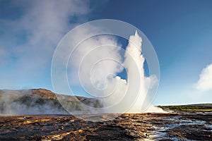 Strokkur geyser eruption in Iceland. Fantastic colors shine through the steam. Beautiful pink clouds in a blue sky