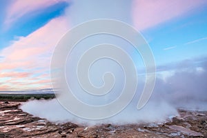 Strokkur geyser eruption in Iceland. Fantastic colors shine through the steam. Beautiful pink clouds in a blue sky