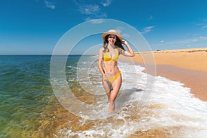 strolling young sexy woman in swimsuit and hat walks along the beach along the sea