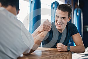 Strong, active and men arm wrestling in the gym on a table while being playful for a challenge. Rivalry, game and male