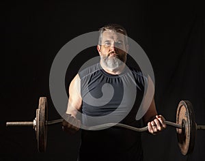 Strong, active, middle aged man with gray beard lifting heavy weights in studio setting