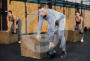 Strong adult man doing jumping exercises over box at cross training style gym. Fit sportsman jump at box in workout gym